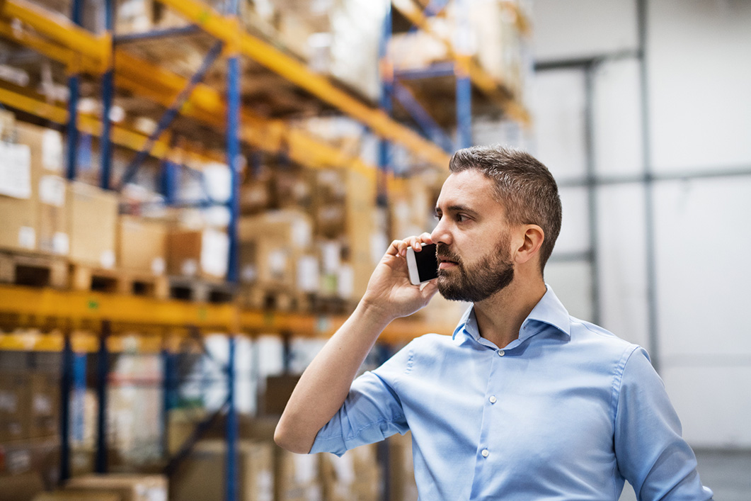 Warehouse worker or supervisor with a smartphone, making a phone call, looking around confused.