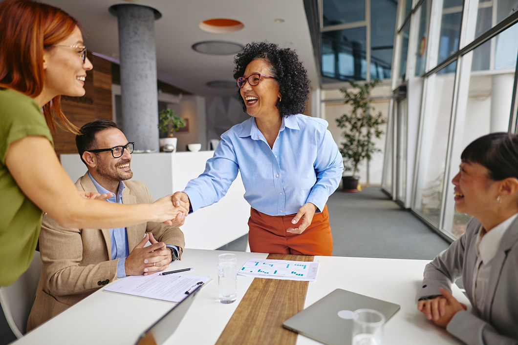 Diverse Team in a Modern Office Setting, two women shaking hands expressing collaboration and success.