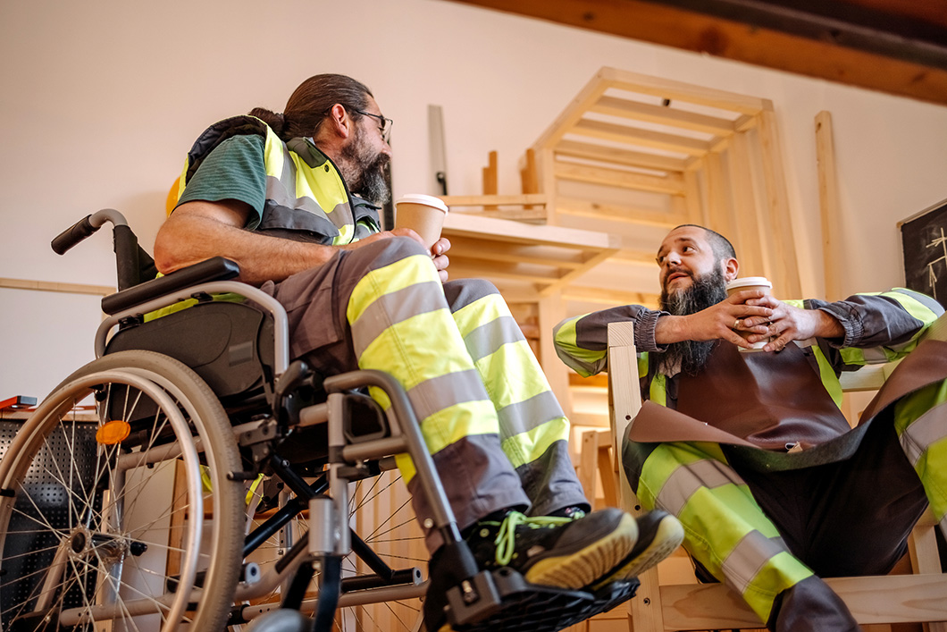 Worker in wheelchair having a coffee break with a colleague in a workshop