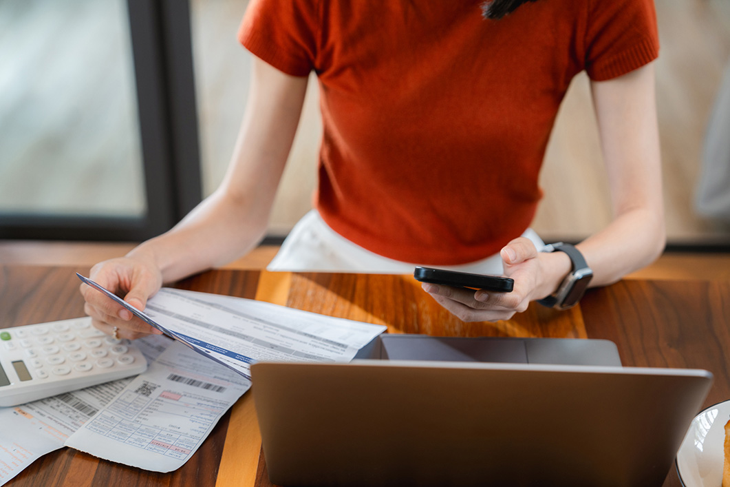 Close-up of woman doing finances on laptop, checking bills and expenses, using calculator with paperwork on the table