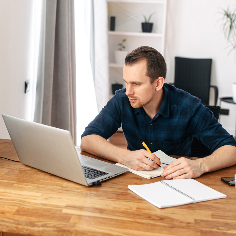 business man sitting at a desk using a laptop to watch e learning whilst taking notes