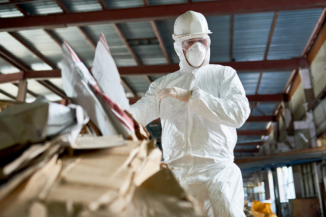 Worker in Hazmat Suit Sorting Cardboard at Industrial Plant
