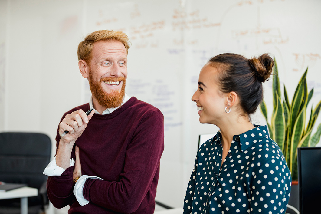 Man and woman talking an laughing with one another while at work at an office.
