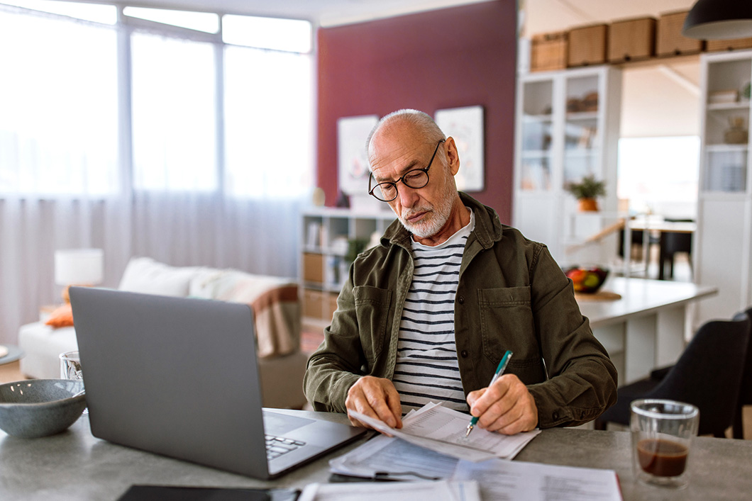 A man sits, working on a laptop, and makes notes.