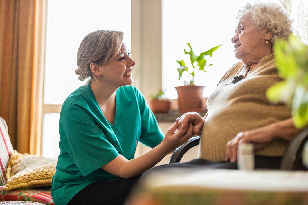 A careworker kneels down and tends to am elderly lady.