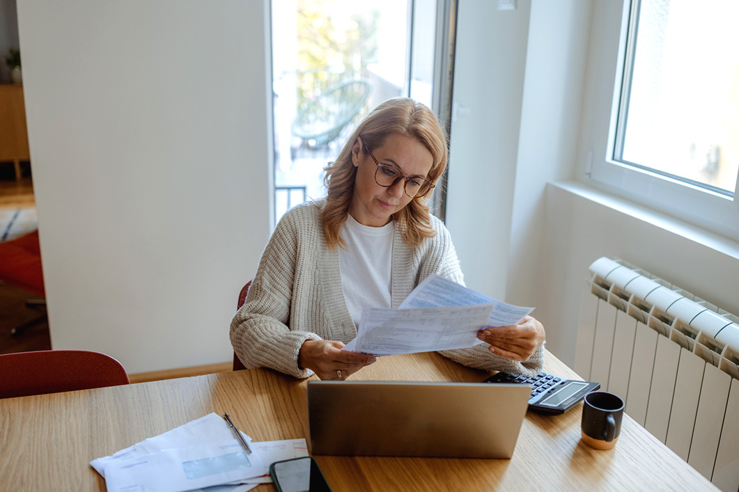 A woman looks at paperwork whilst on a laptop