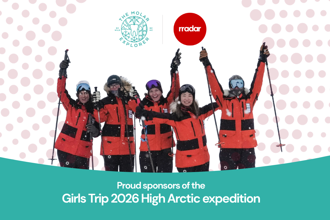 The five female explorers in their cold weather gear raise their arms in celebration.