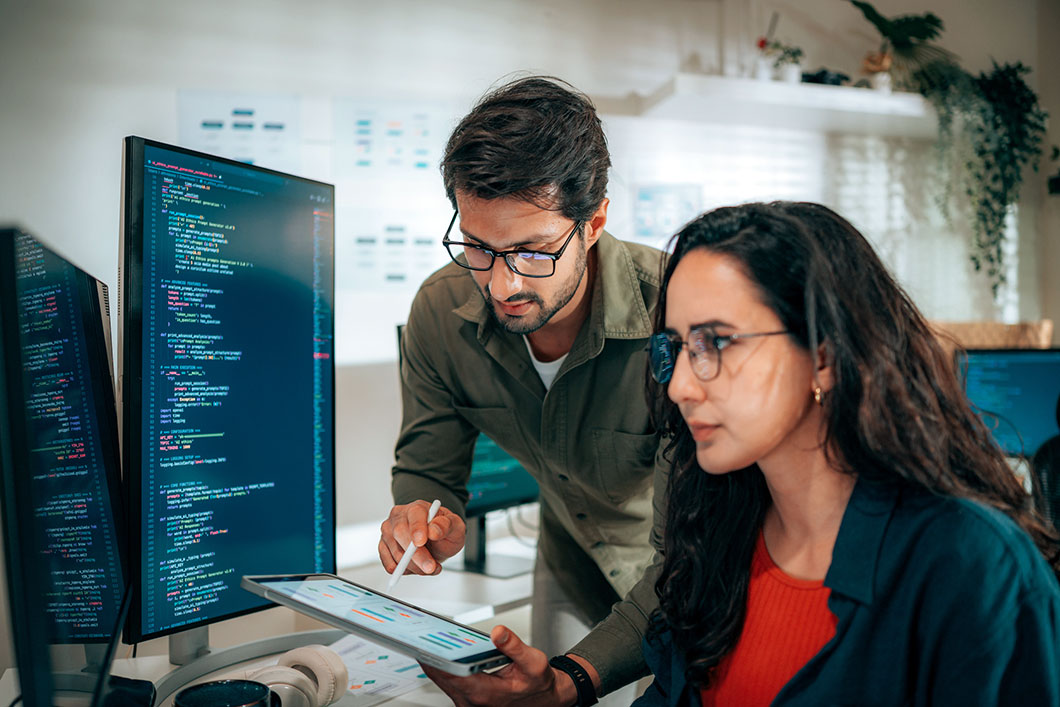 Two colleagues look at code on a computer