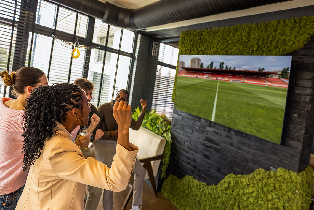 Group of colleagues watching a football match on TV, cheering, celebrating, and enjoying the game together in a lively sports atmosphere.
