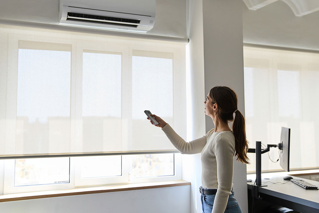 A woman in a workplace operates an air conditioning unit.