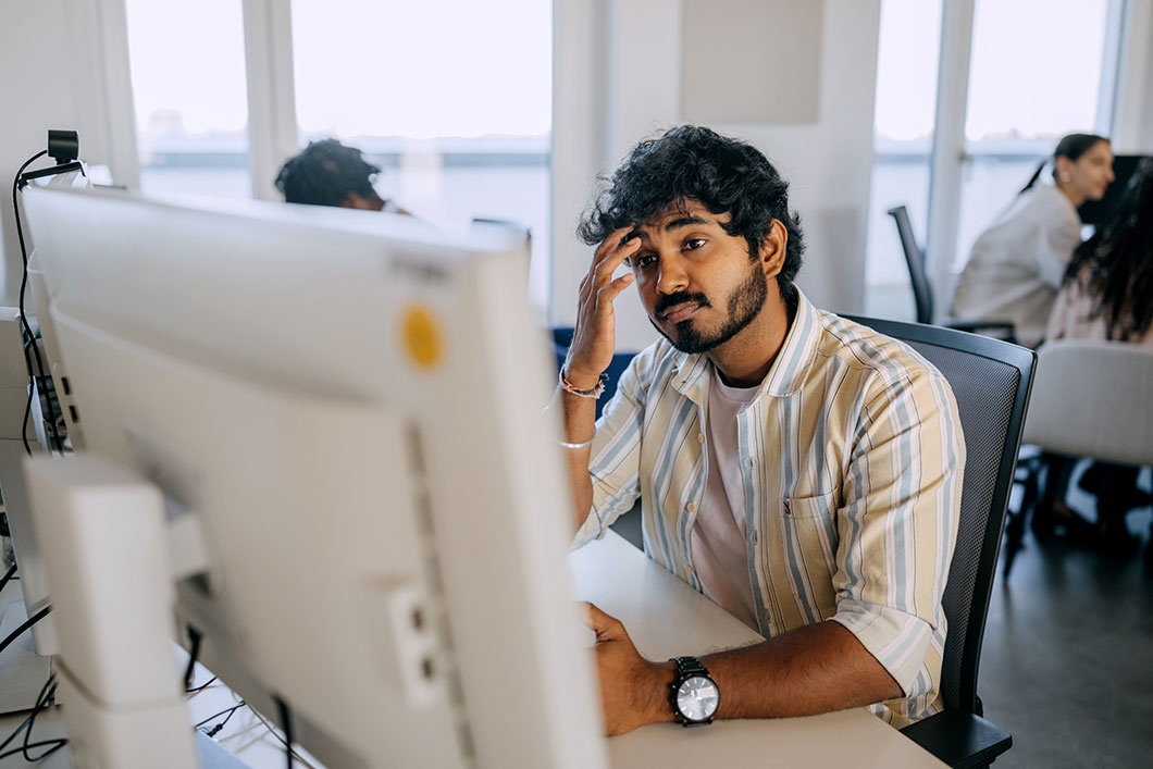 A worker on a computer holds his head in a tired way.