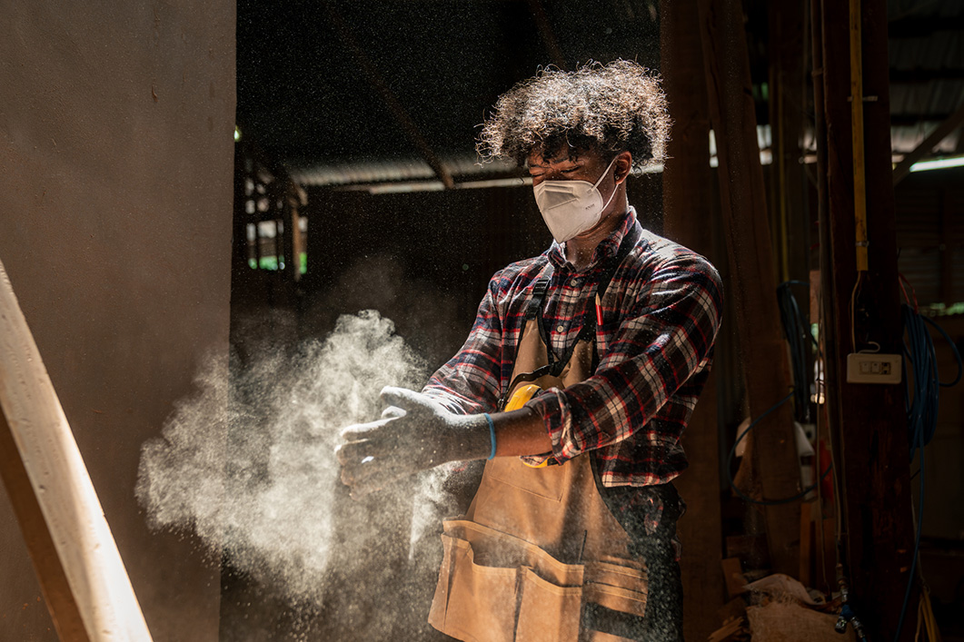 A worker in ppe wit dust flying off their hands.