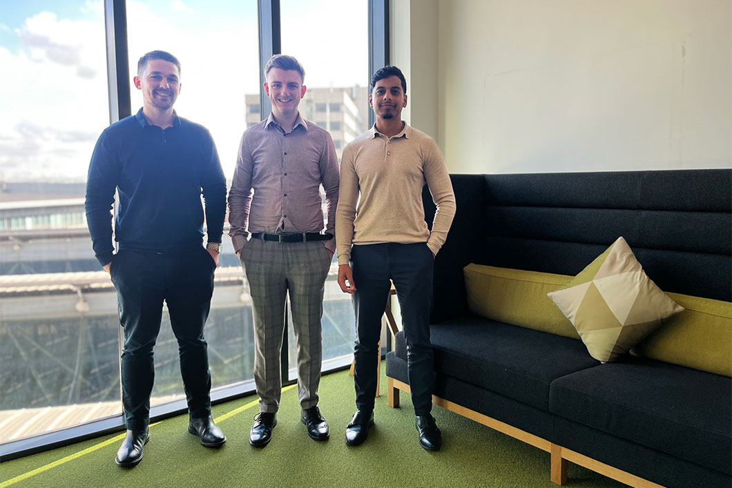 The three trainees stand in front of a window